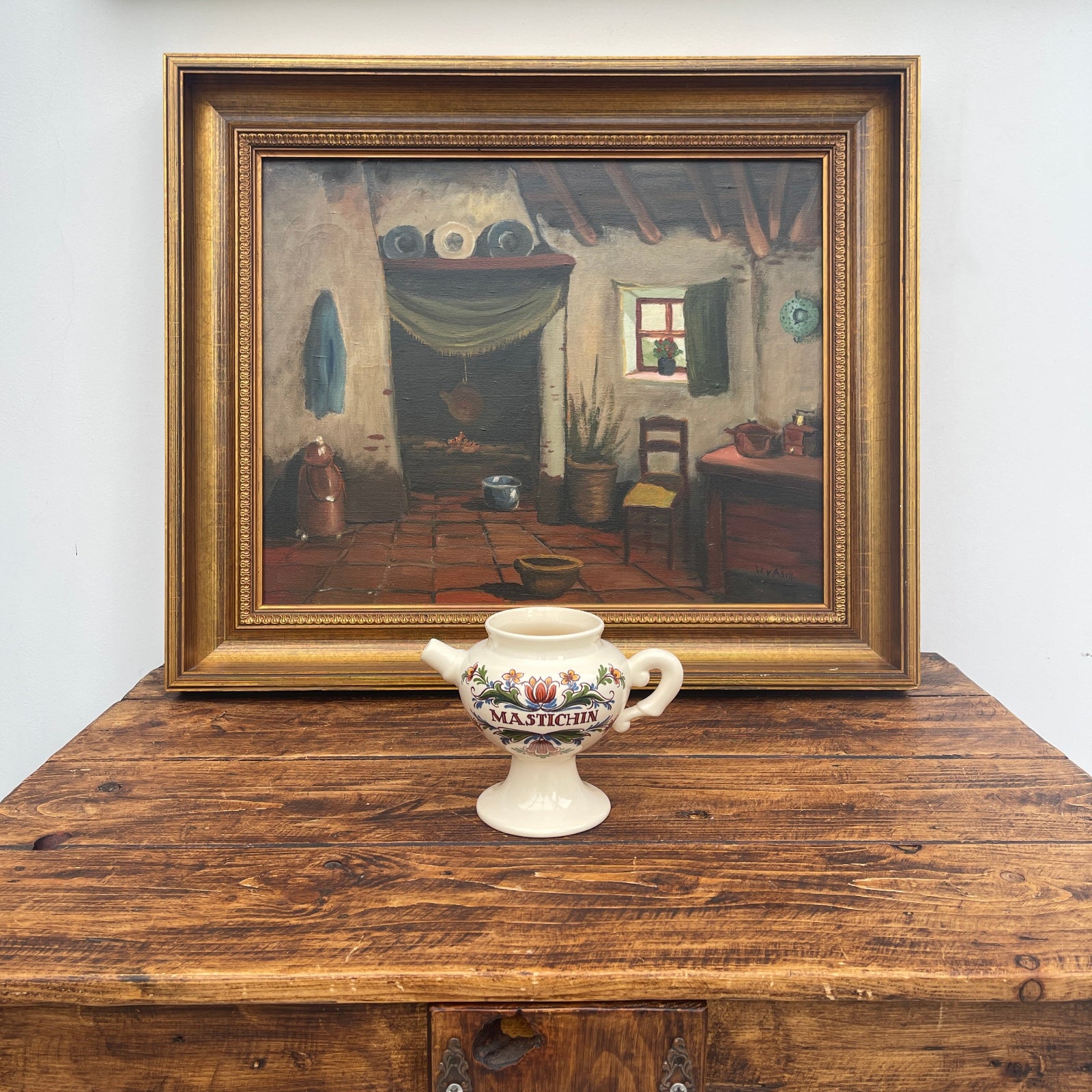 Framed painting of a rustic interior scene on a wooden surface with a decorative ceramic mug.