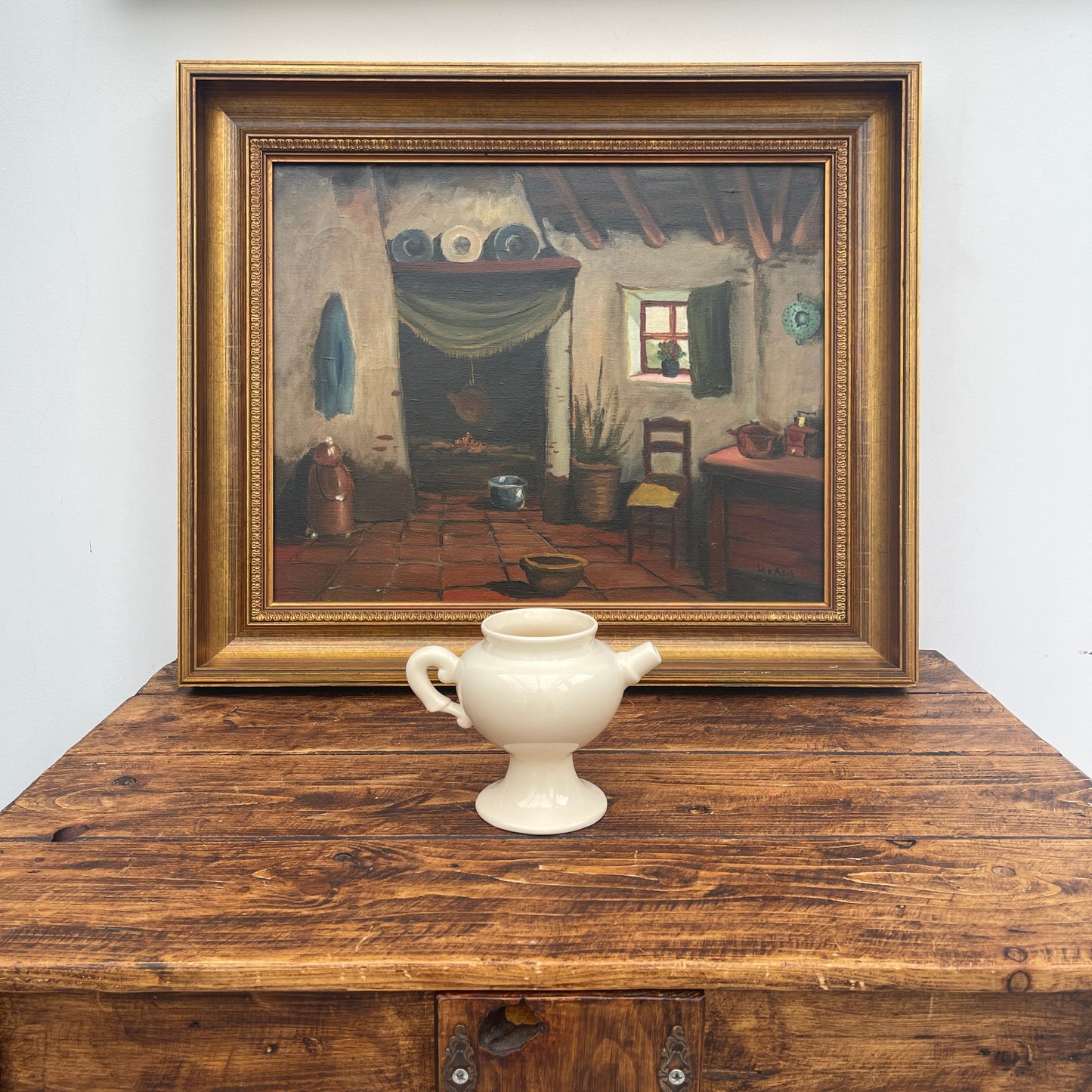 Framed painting of a room scene on a wooden surface with a white vase.