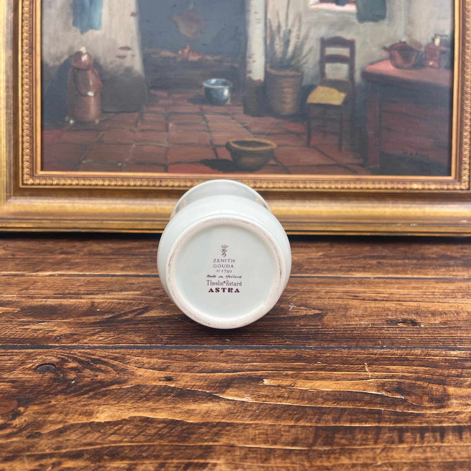 Small white container with text on a wooden surface in front of a framed painting