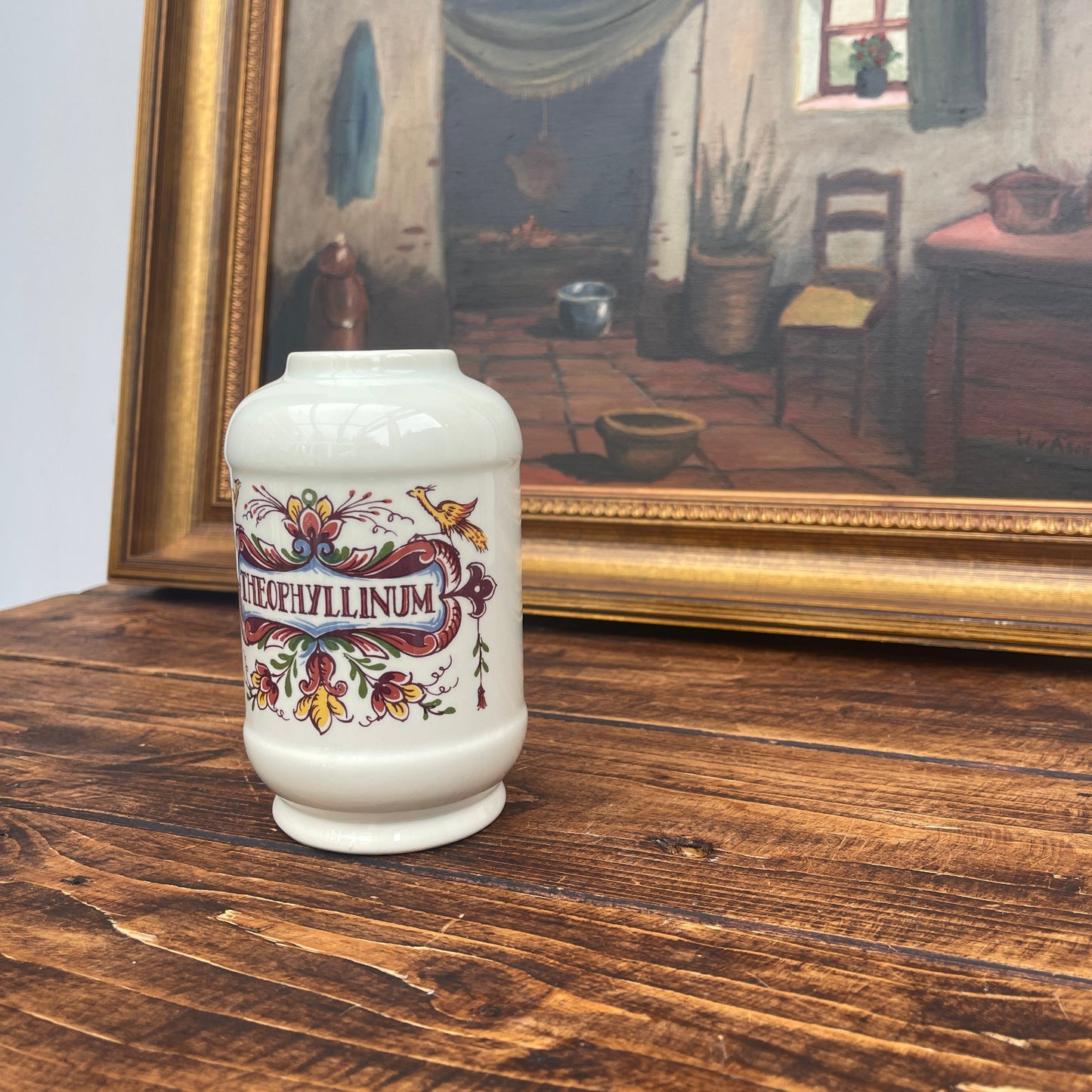 Decorative vase with floral design on a wooden surface in front of a framed painting.