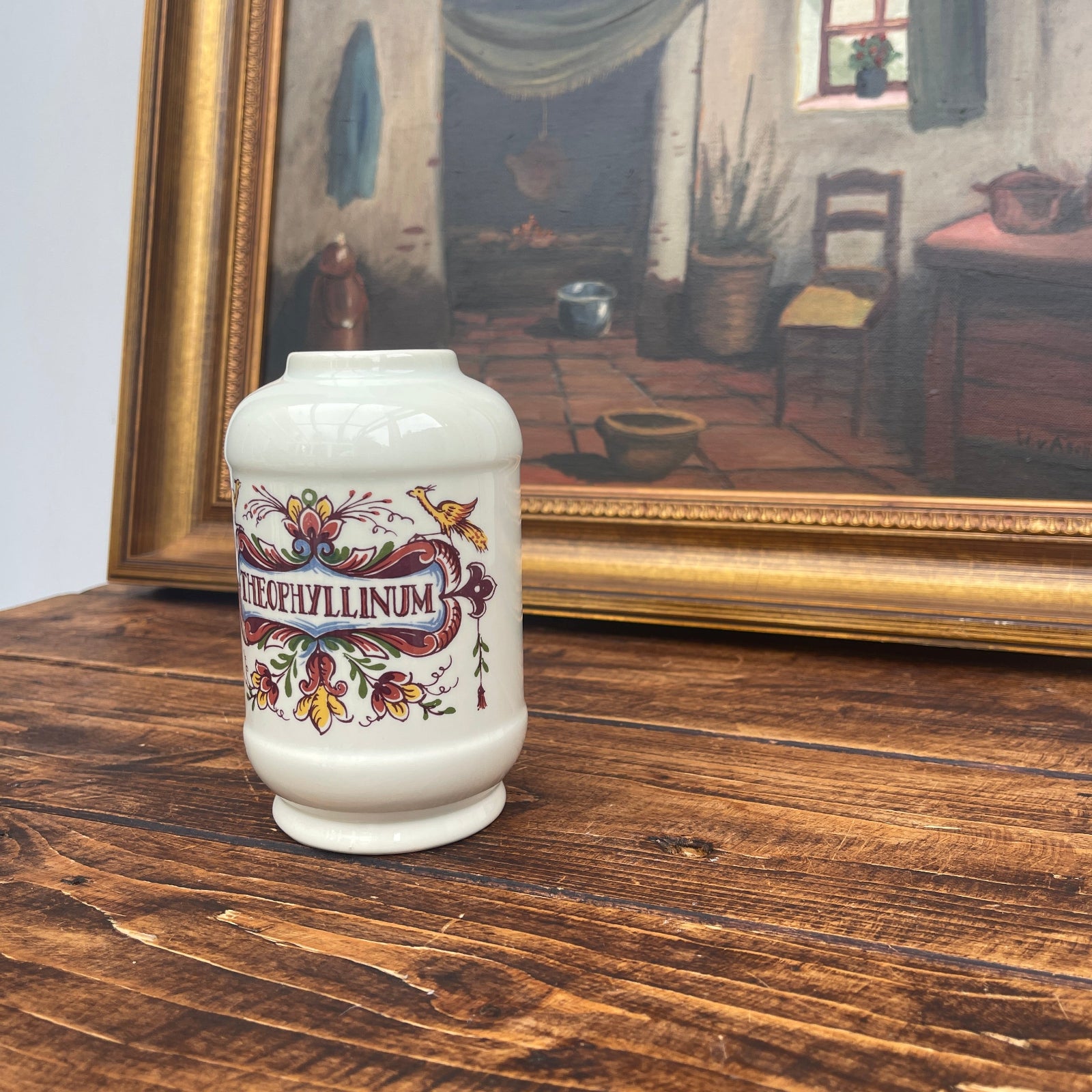 Decorative vase with floral design on a wooden surface in front of a framed painting.