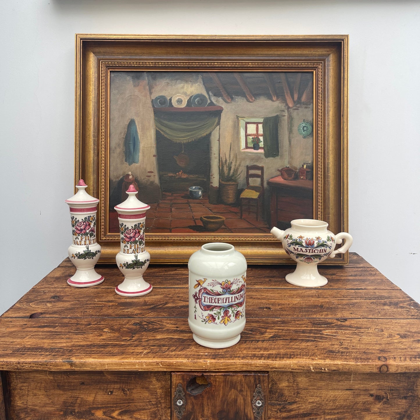 Decorative vases with floral designs on a wooden surface, framed painting in the background.