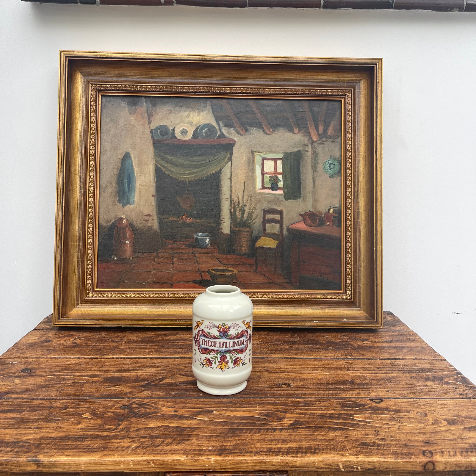Framed painting of a rustic interior scene on a wooden surface with a decorative vase.