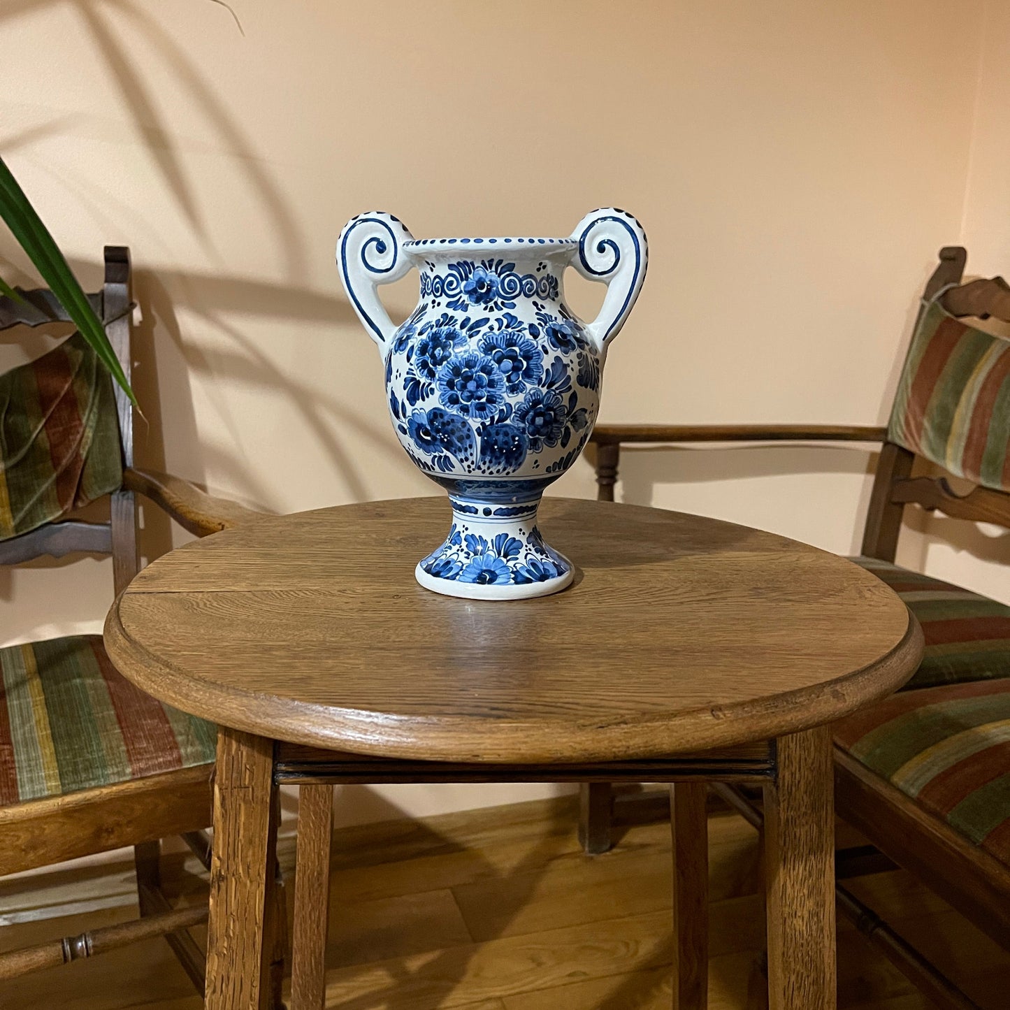 Blue and white floral-patterned vase on a wooden table with chairs in the background.