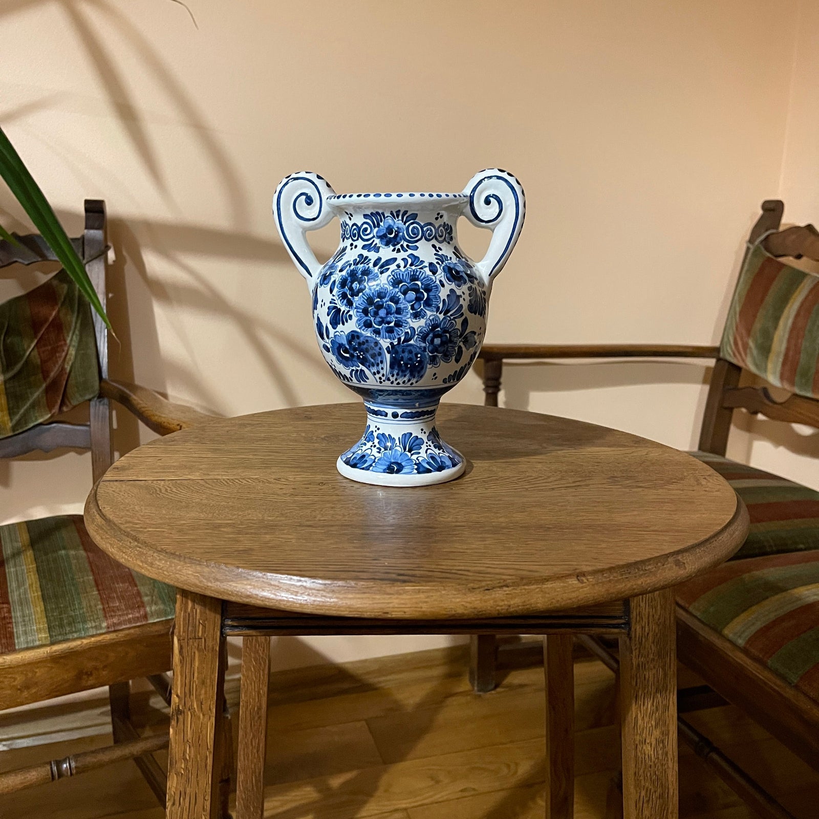 Blue and white floral-patterned vase on a wooden table with chairs in the background.