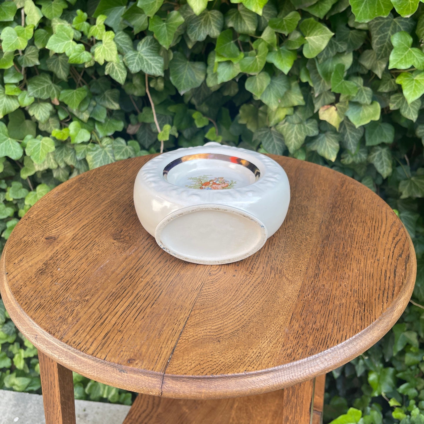 White ceramic ashtray on a wooden table with green foliage in the background