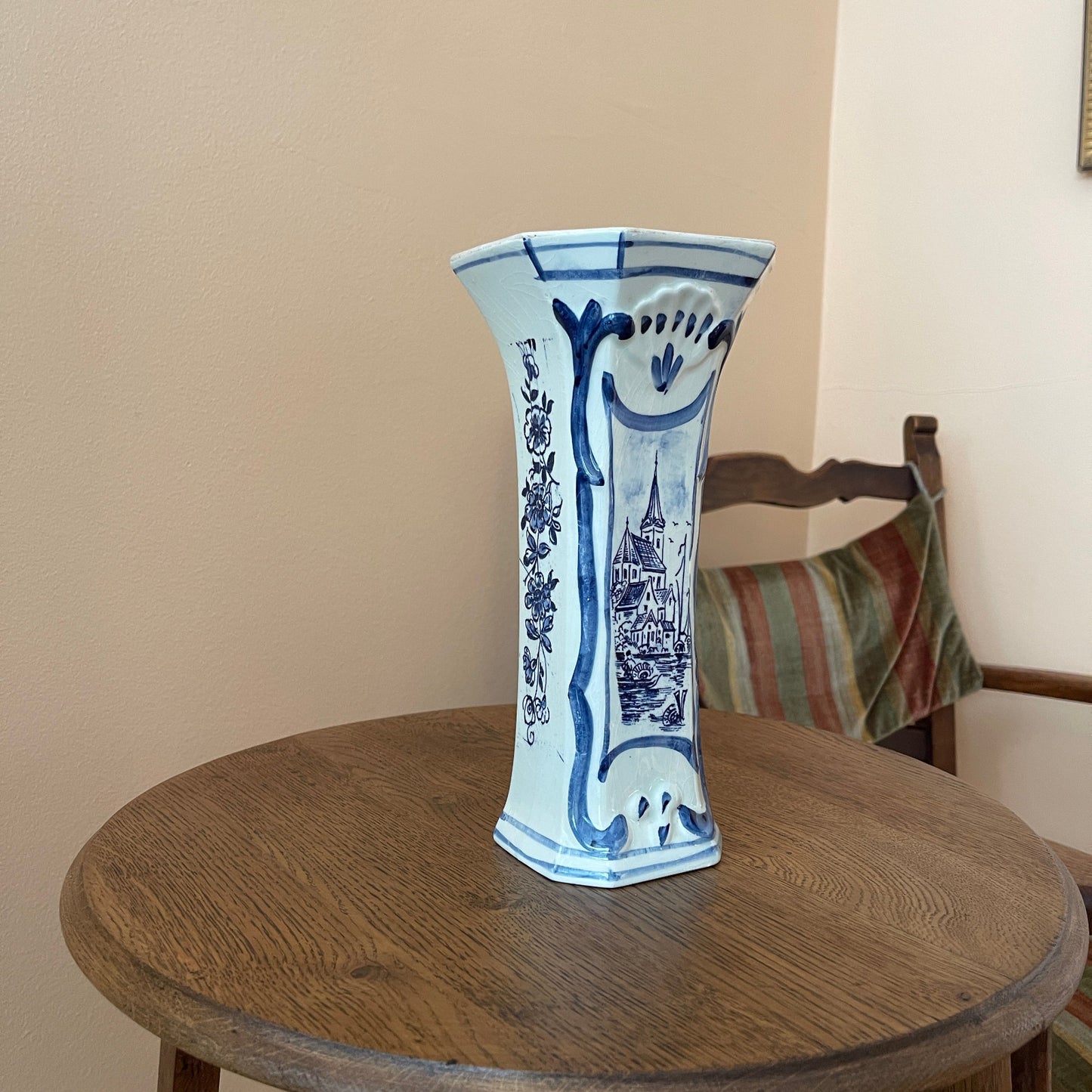 Blue and white decorative vase on a wooden table with a chair and striped cloth in the background.