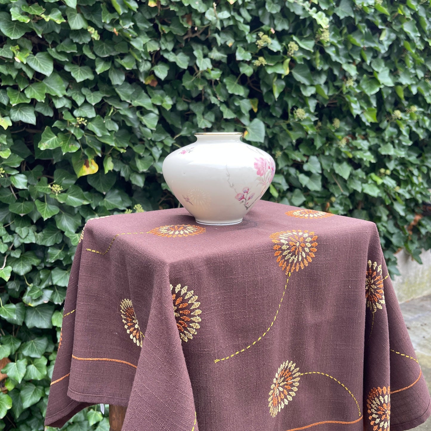 Tablecloth with floral patterns on a table against a green hedge background