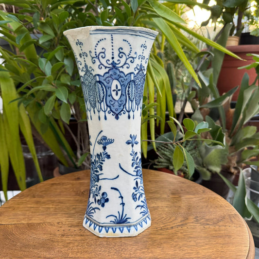 Ceramic vase with blue floral patterns on a wooden surface with plants in the background