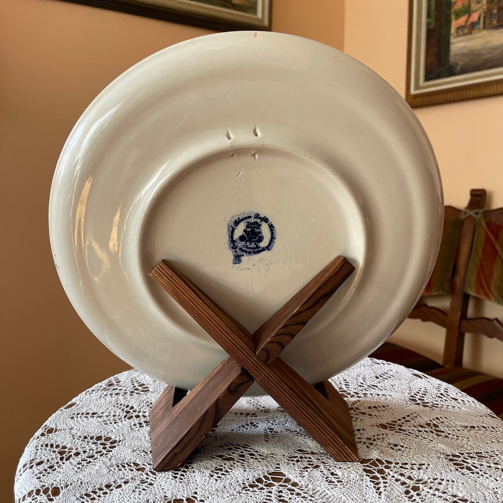 White ceramic plate with a blue design on a wooden stand on a lace tablecloth.