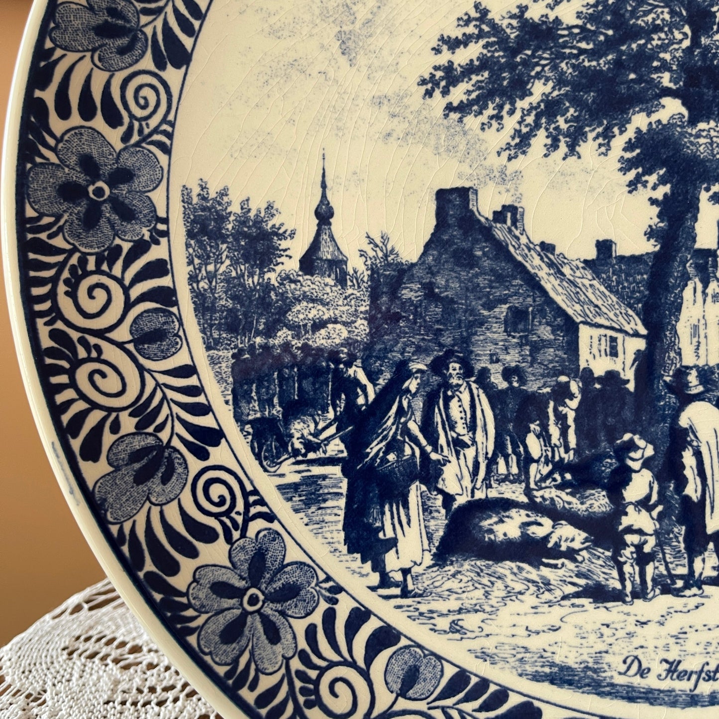 Decorative plate with a black and white scene of people in a village and floral patterns.