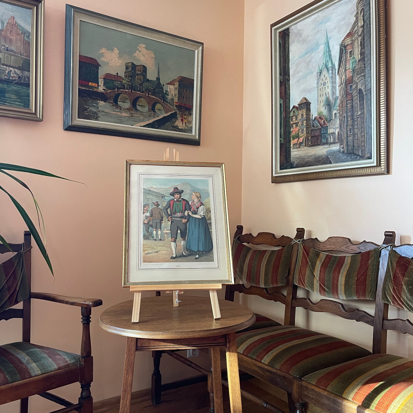 Room interior with framed paintings on a wall, wooden chairs with striped cushions, and a small round table.