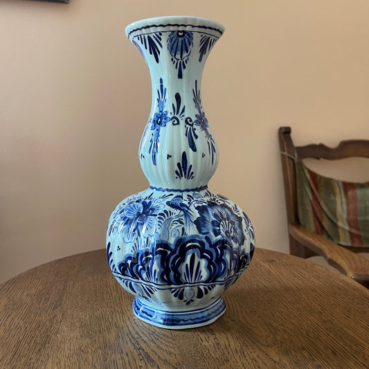 Blue and white floral-patterned vase on a wooden table with a chair in the background.