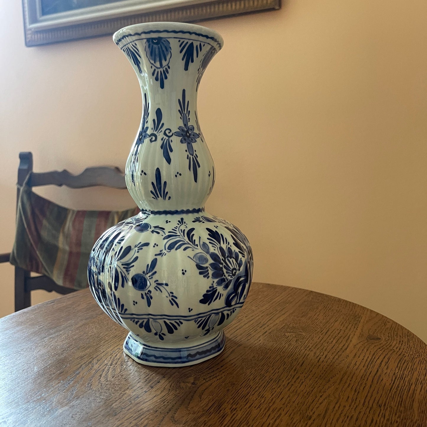 Blue and white floral-patterned vase on a wooden table with a chair and wall in the background.