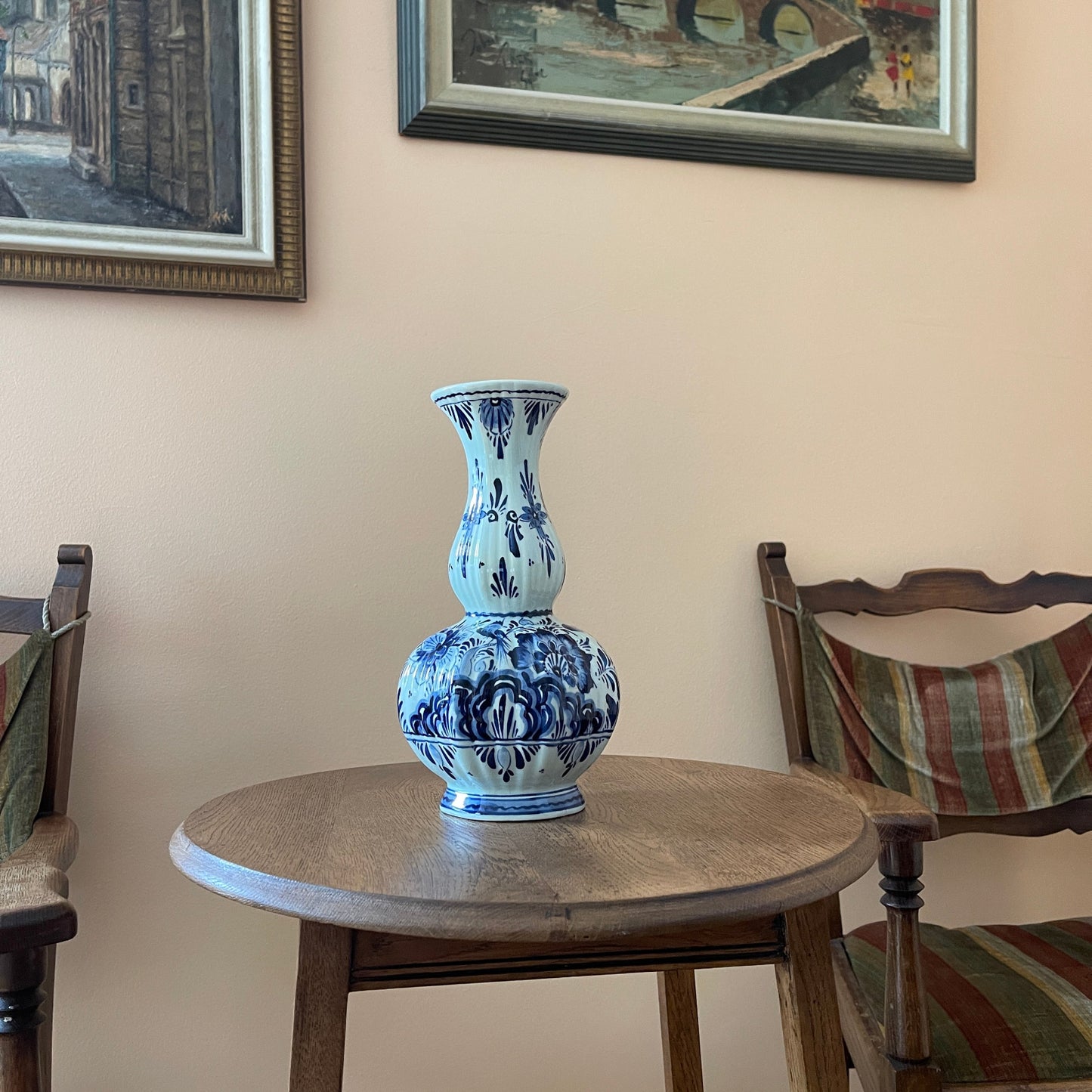 Blue and white vase on a wooden table with framed pictures on the wall.