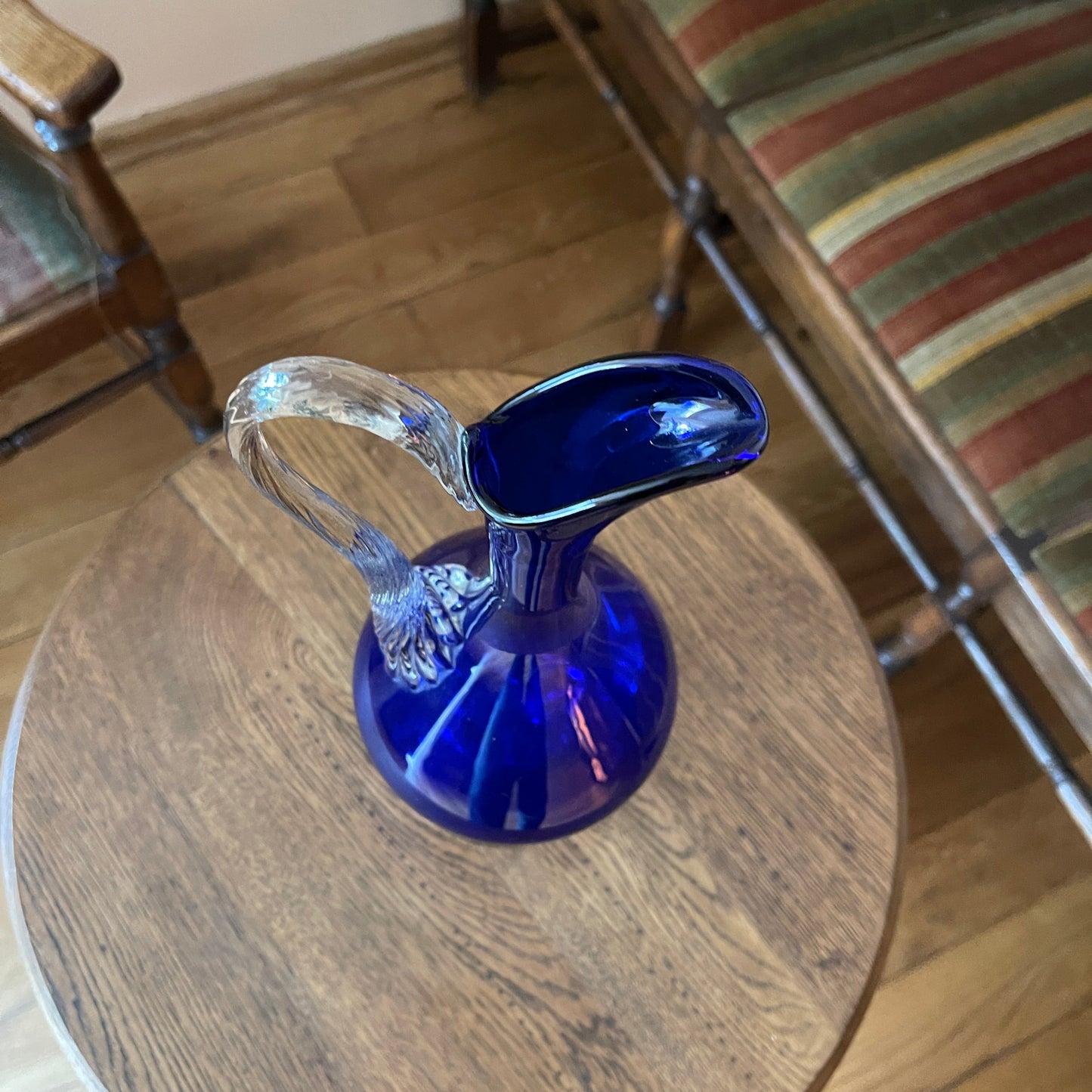 Blue glass pitcher on a wooden table with a chair in the background
