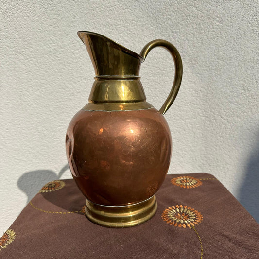 Copper and brass pitcher on a textured surface with a neutral background