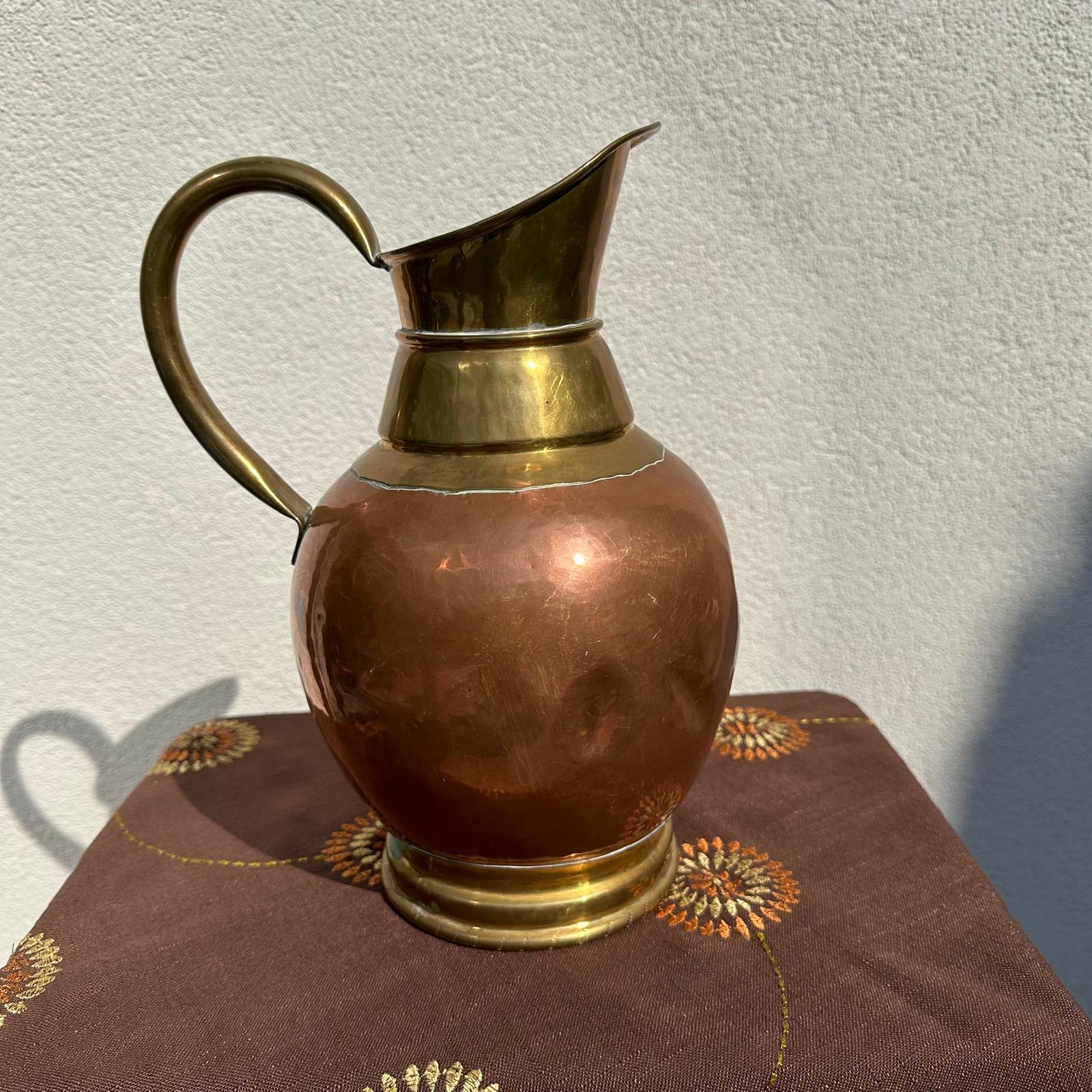 Copper and brass pitcher on a textured surface with a neutral background