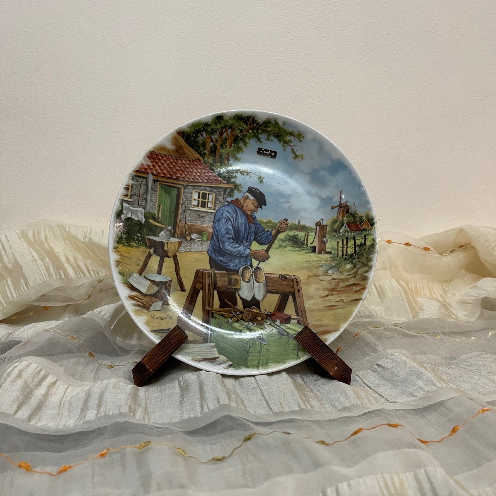 Decorative plate with a painted scene of a man working on a farm, placed on a fabric surface.