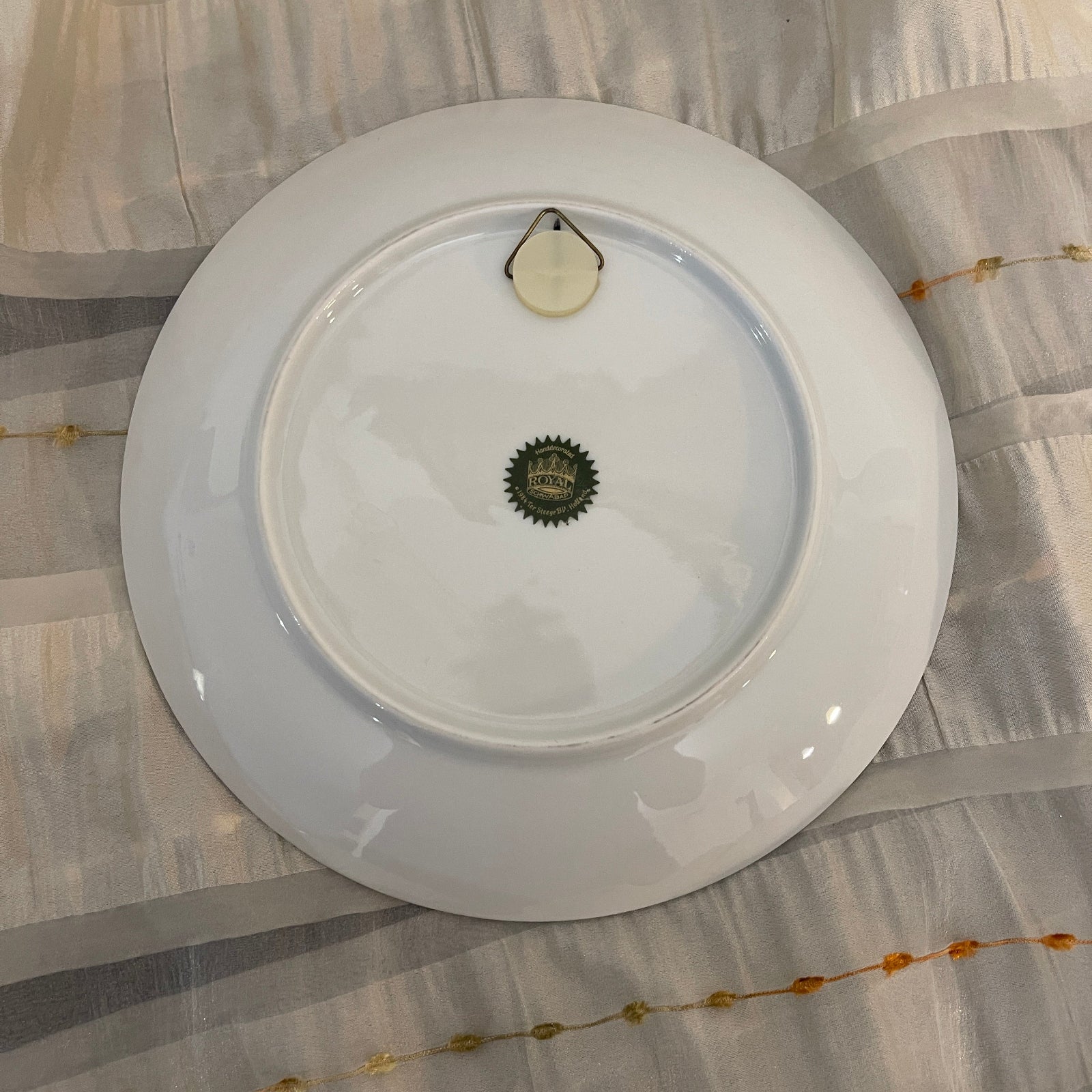White plate with a brand logo on a patterned fabric background