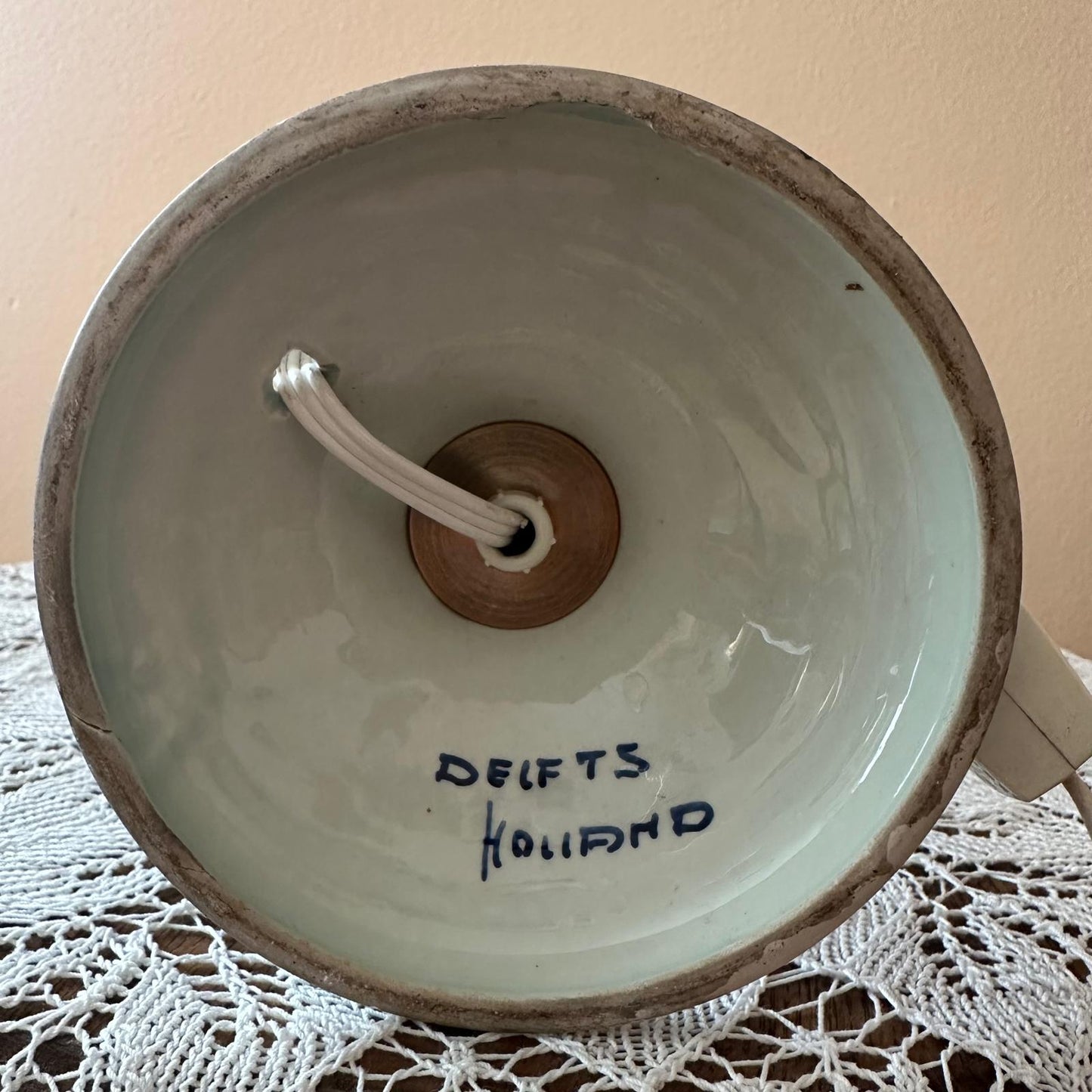 Ceramic bowl with wooden handle and 'Delfts Holland' inscription on a lace tablecloth.