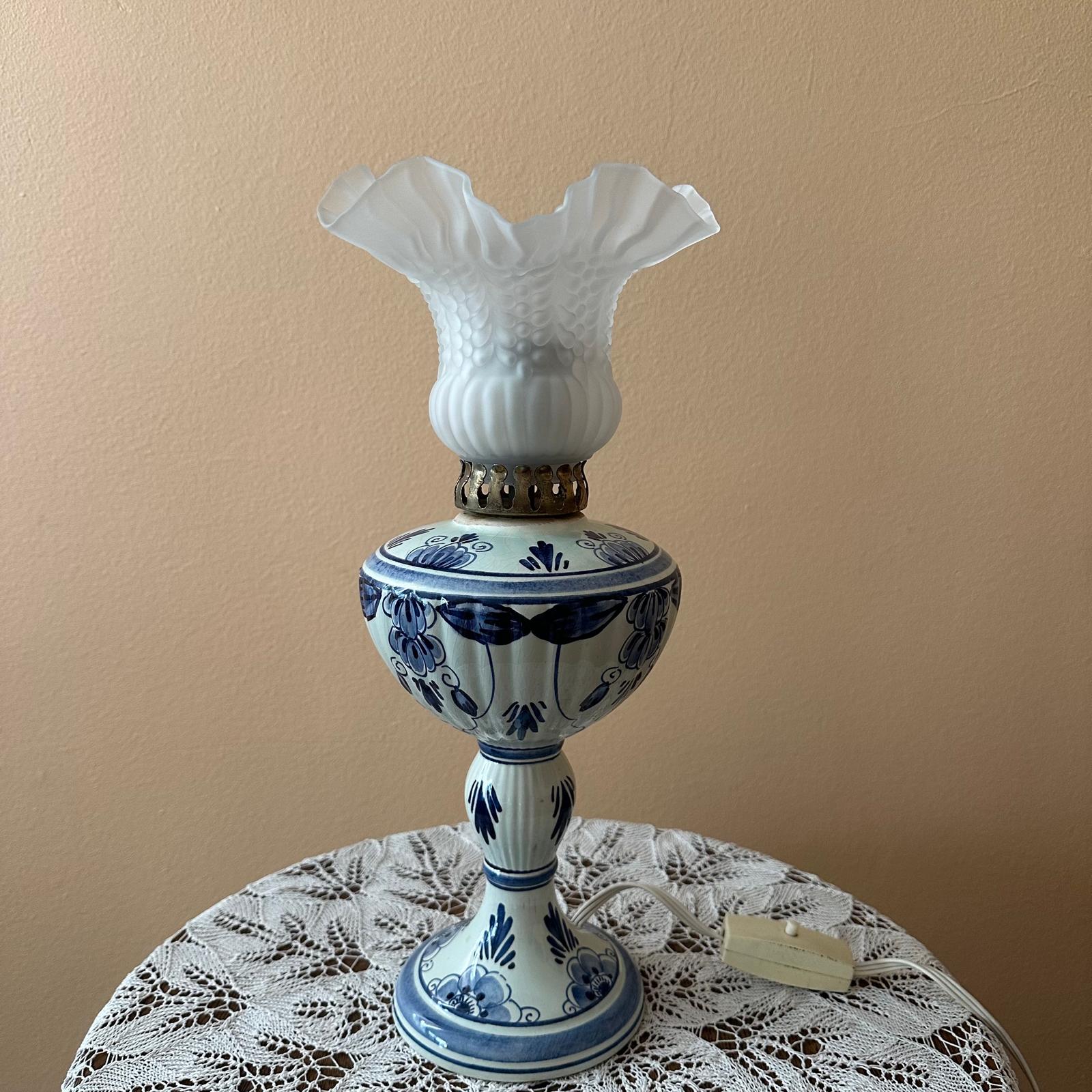 Decorative lamp with blue floral patterns on a lace tablecloth against a beige wall.