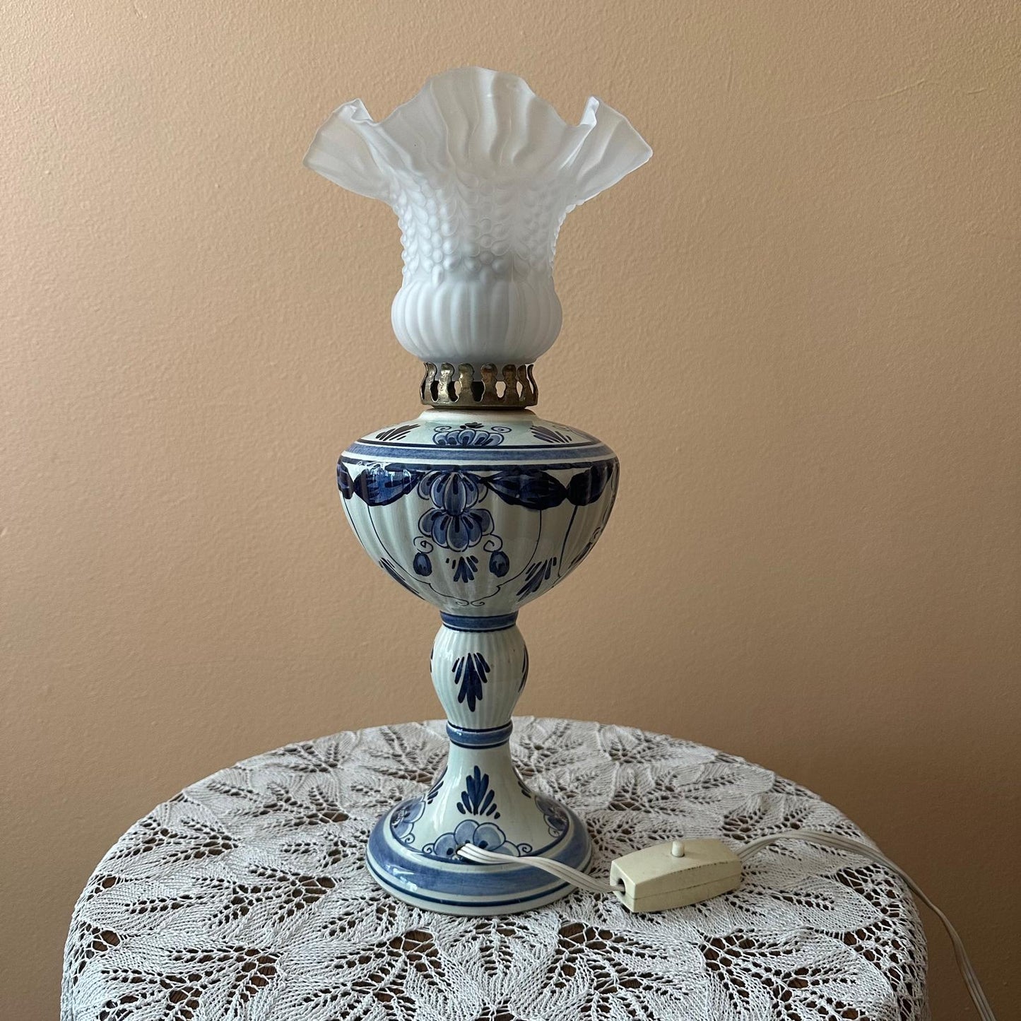 Decorative lamp with blue floral patterns on a lace tablecloth against a beige wall