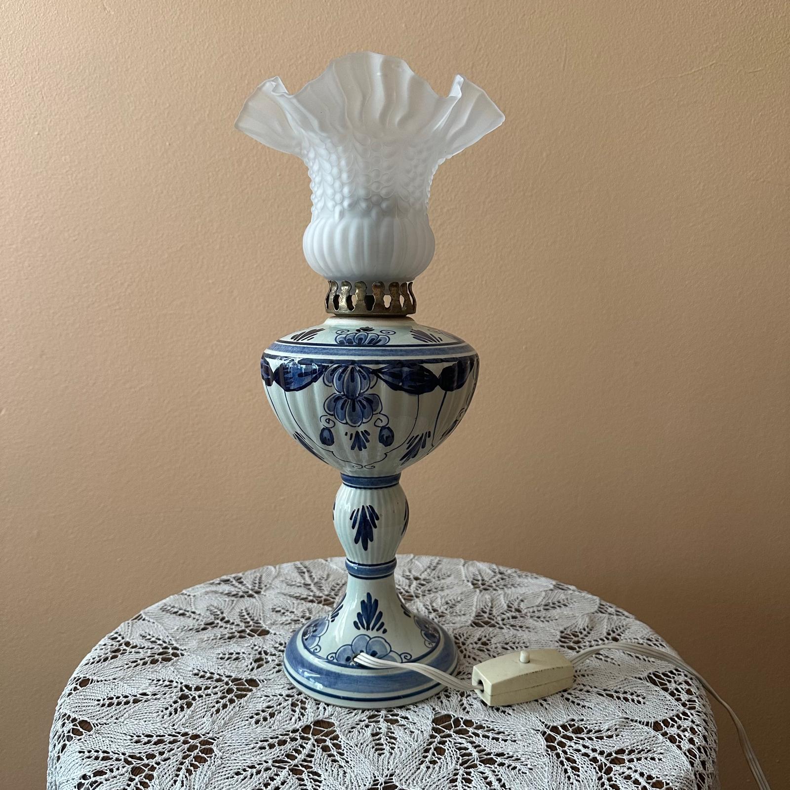 Decorative lamp with blue floral patterns on a lace tablecloth against a beige wall