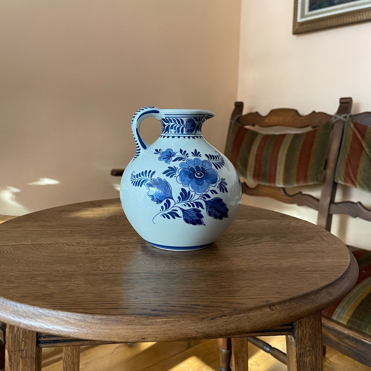 Blue floral-patterned ceramic vase on a wooden table with a chair and striped cushion in the background.