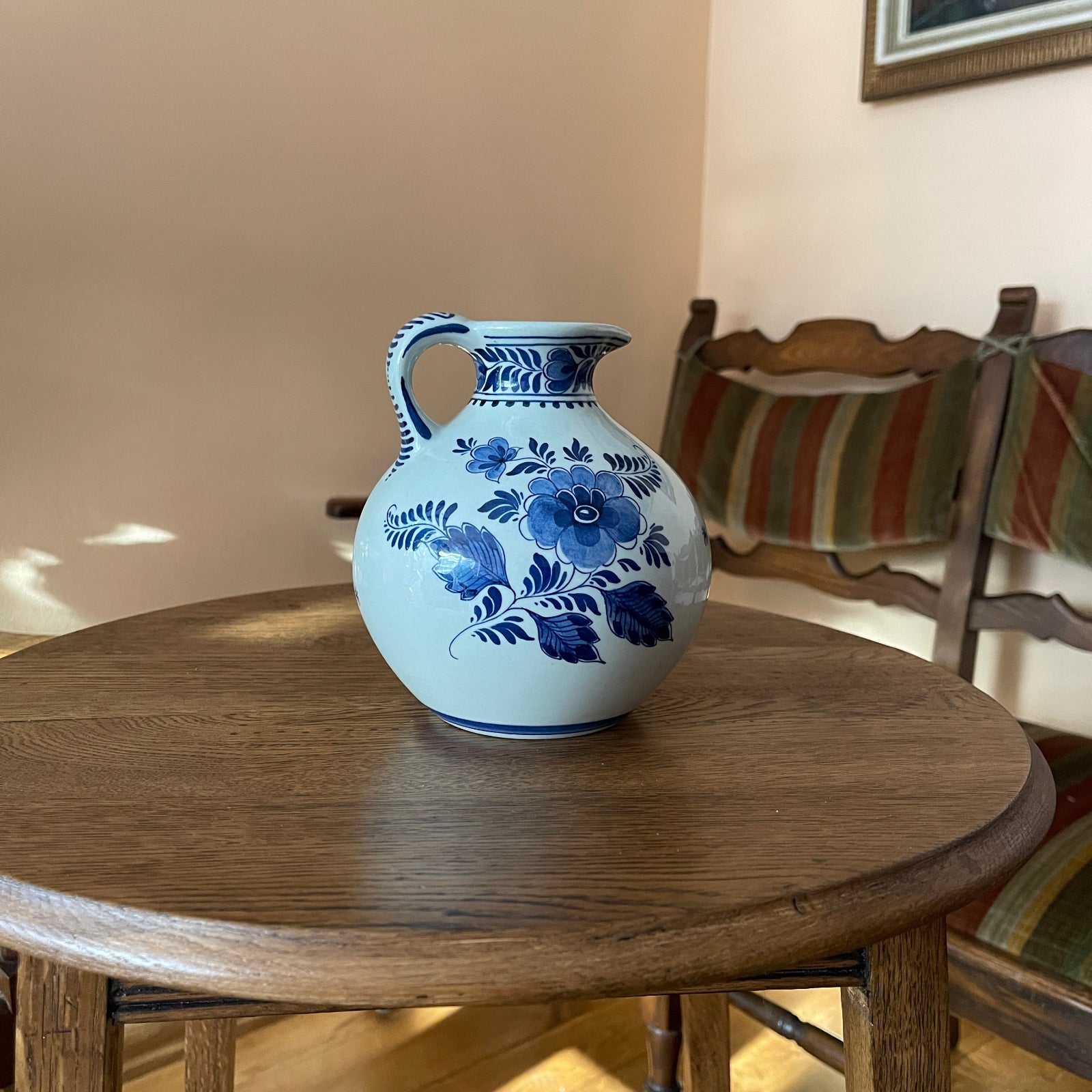 Blue floral-patterned ceramic vase on a wooden table with a chair and striped cushion in the background.