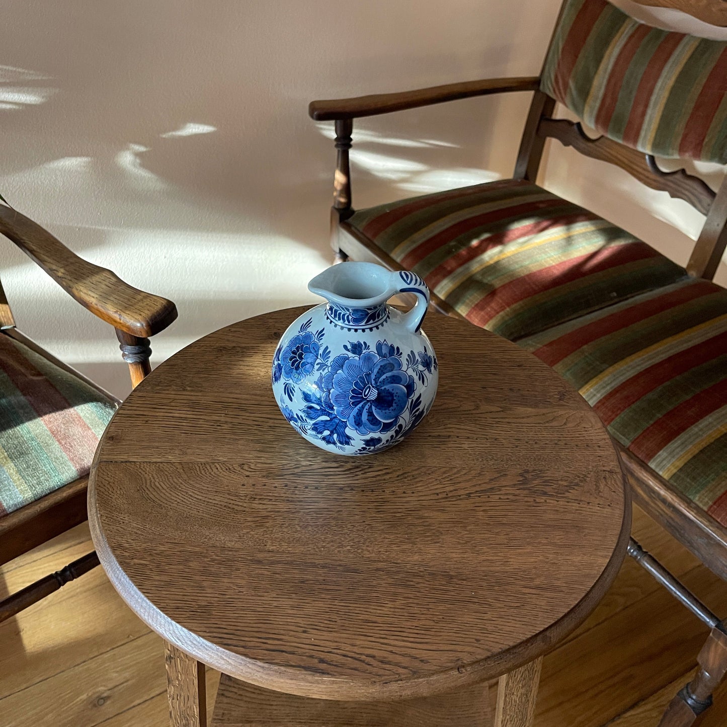 Blue and white floral-patterned pitcher on a wooden table with striped chairs in the background.