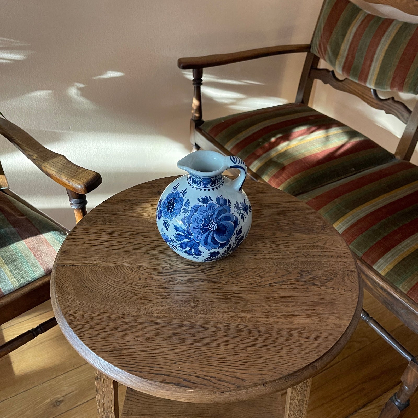 Blue and white floral-patterned pitcher on a wooden table with striped chairs in the background.