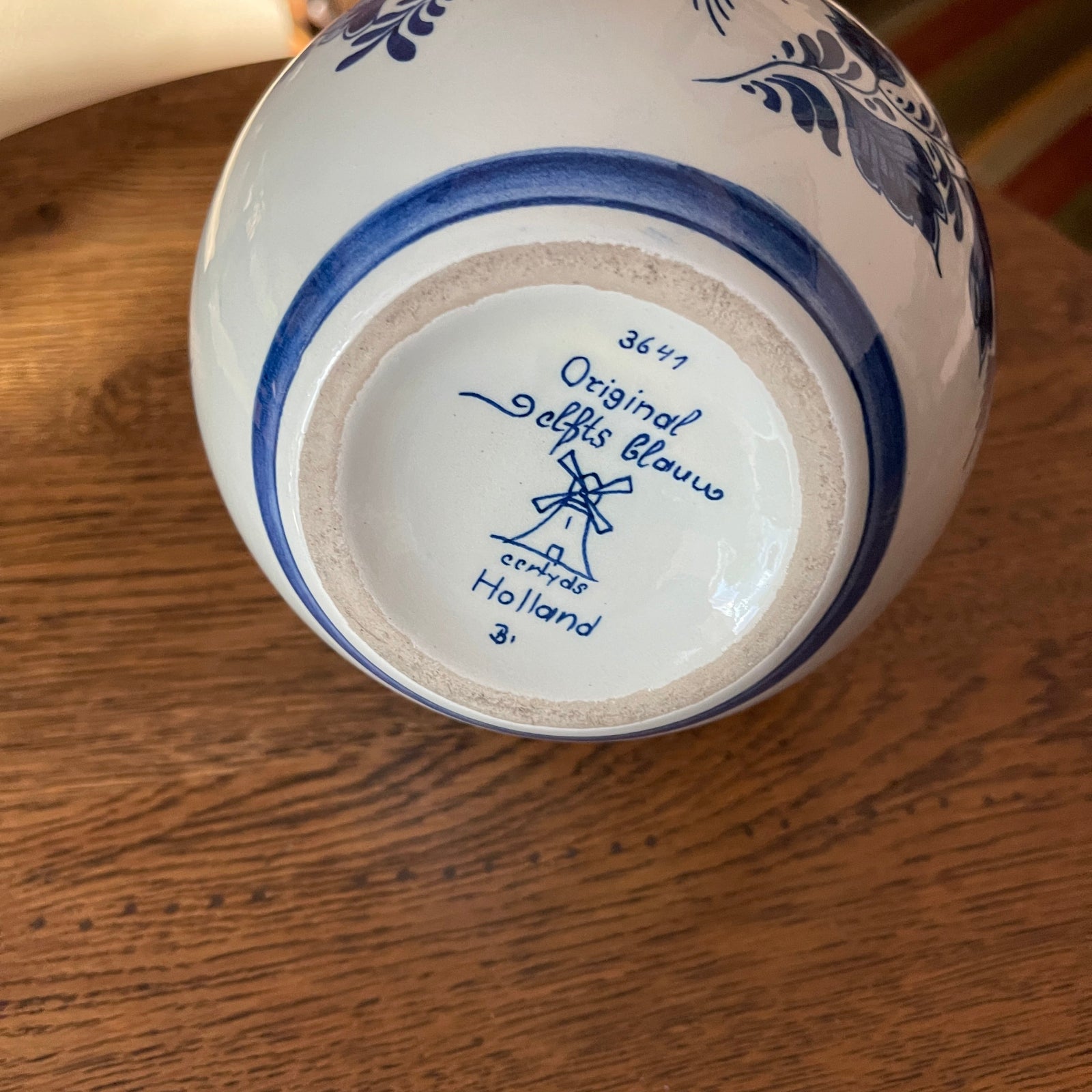 Ceramic vase with blue floral patterns on a wooden surface, showing 'Original Delfts Blauw' branding.