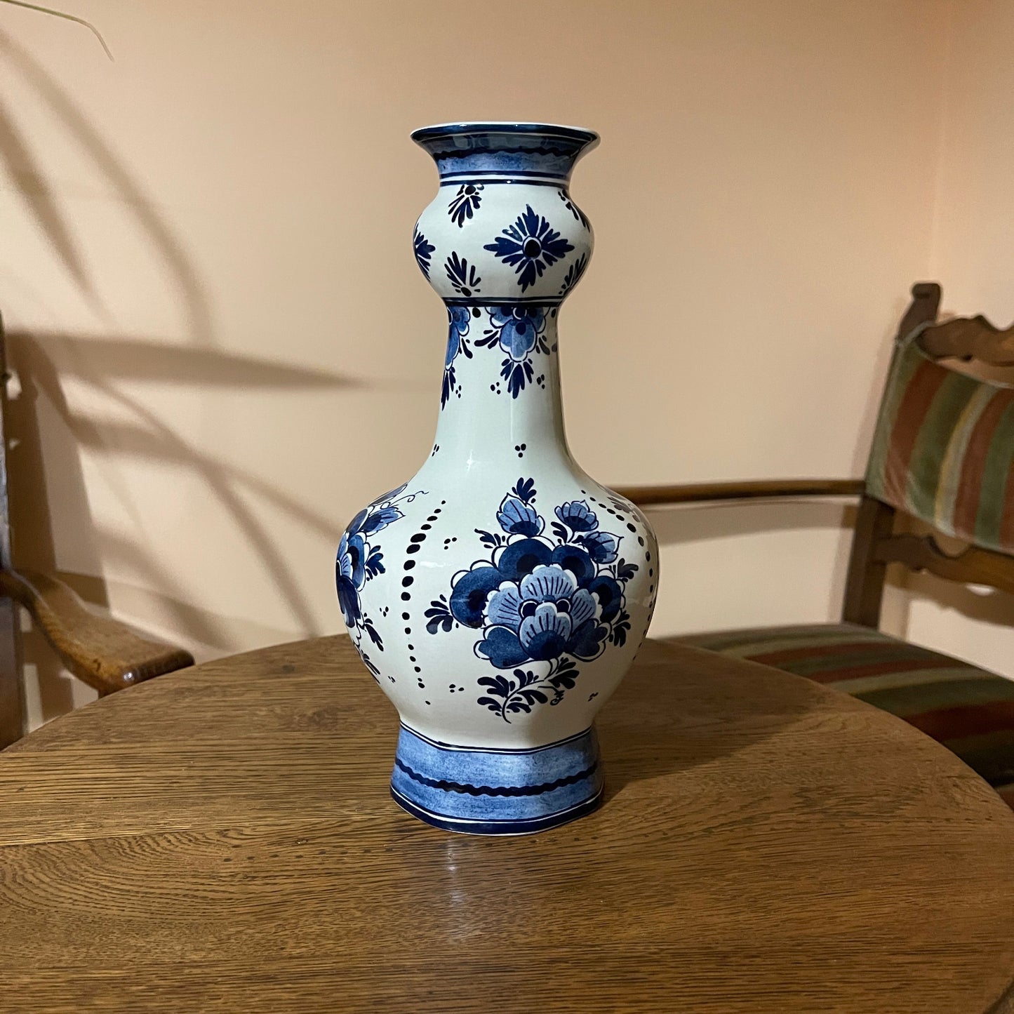 Blue and white floral-patterned vase on a wooden table with a chair in the background.