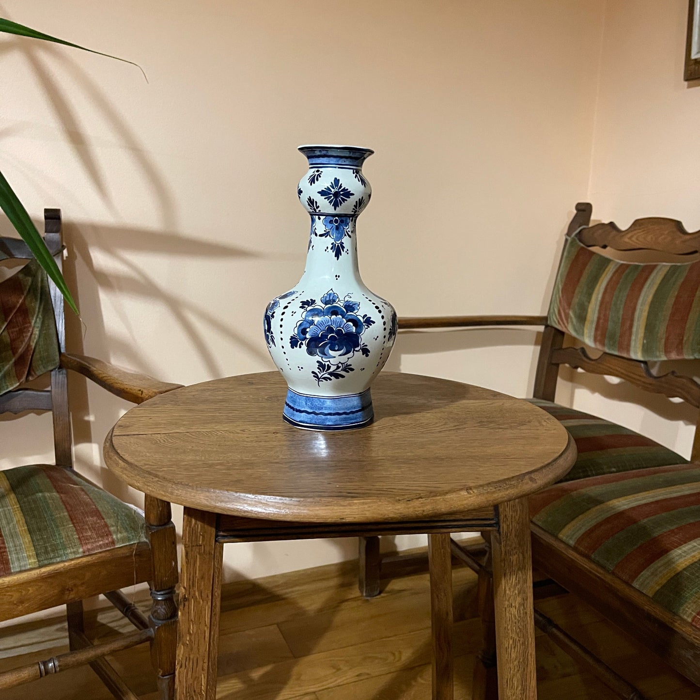 Blue and white floral-patterned vase on a wooden table with two chairs in a room.
