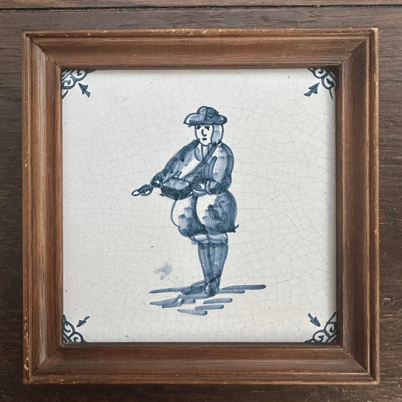Framed artwork of a blue and white ceramic tile with a decorative design on a wooden surface.