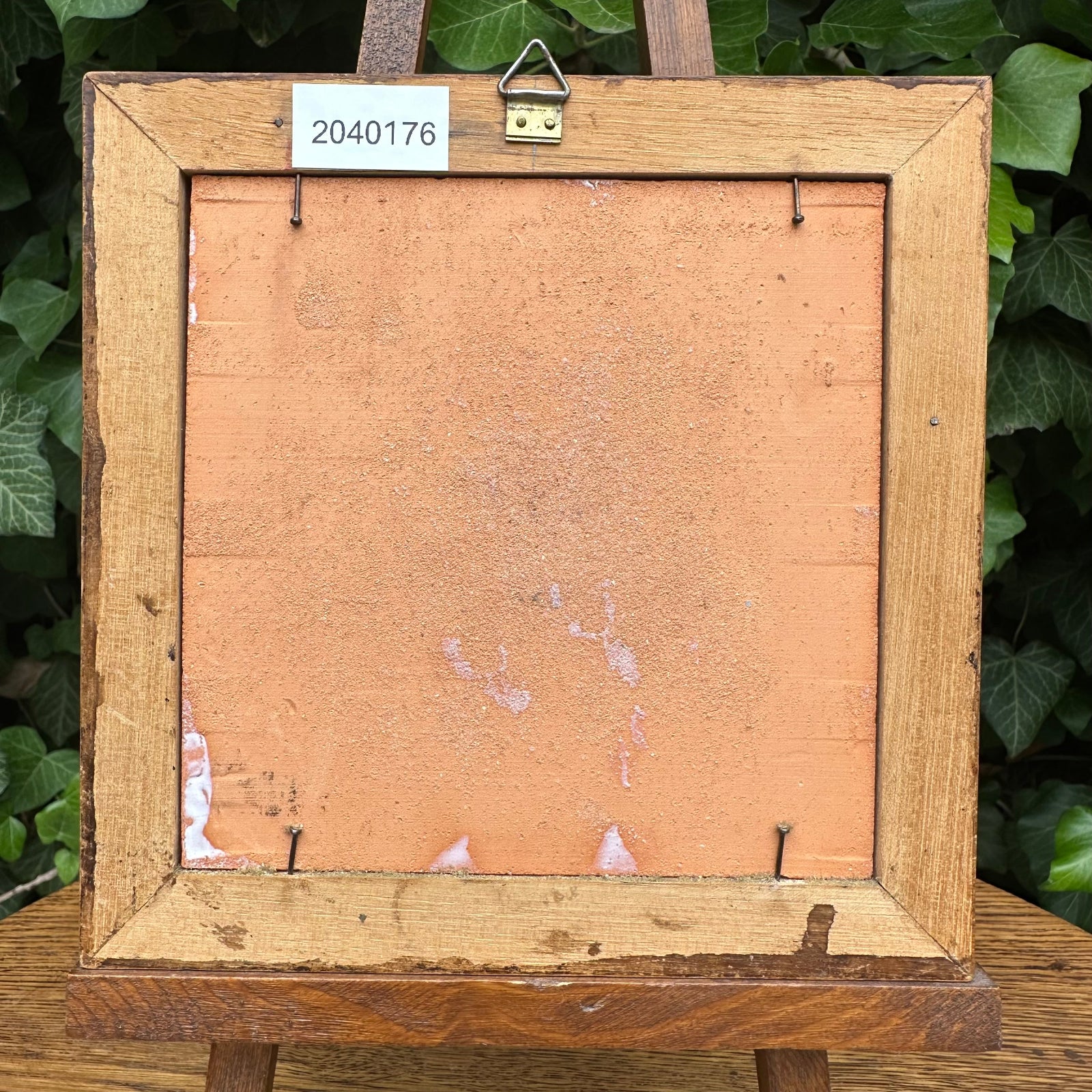 Wooden picture frame with a label on a wooden easel against a green leafy background