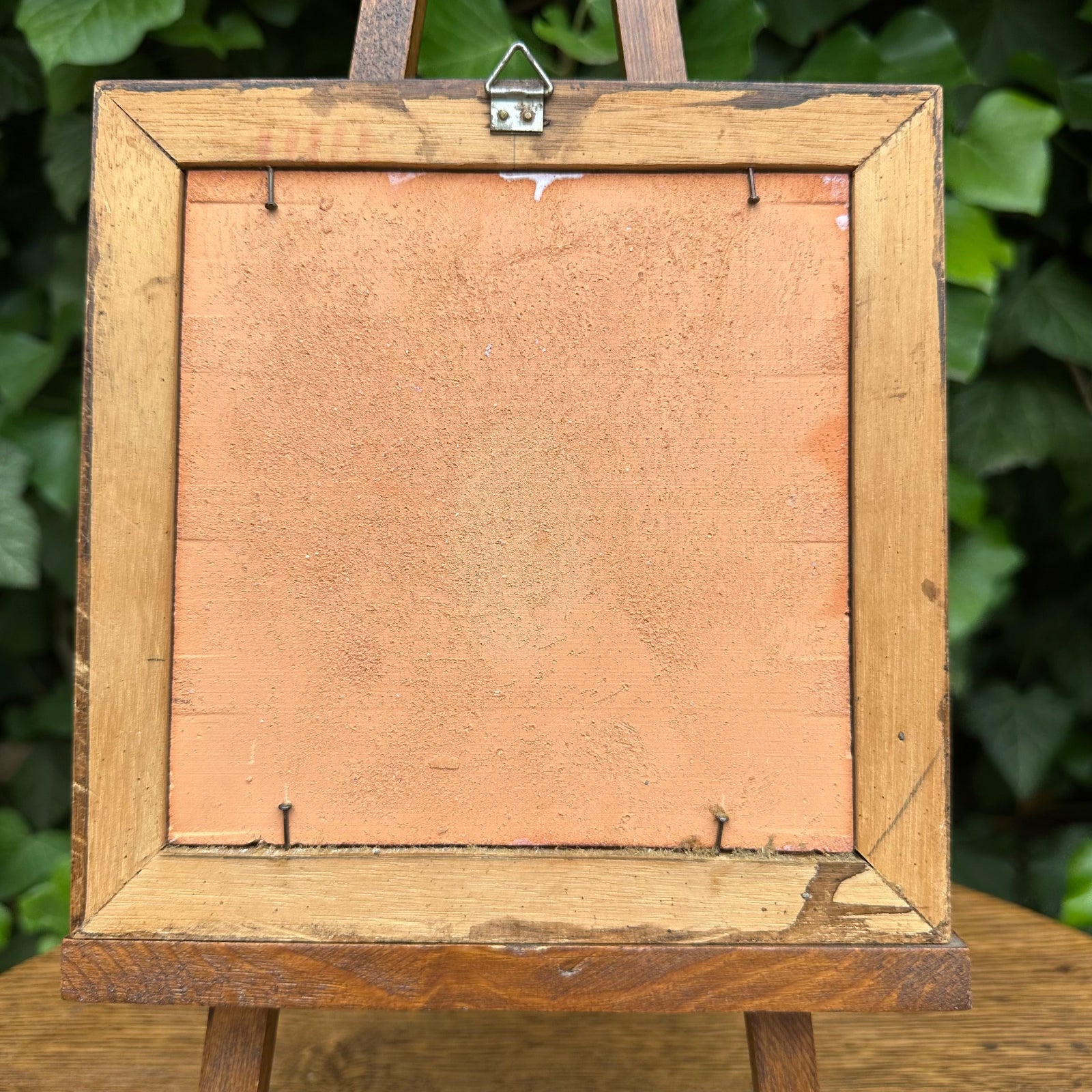 Back view of a wooden picture frame with a green leafy background