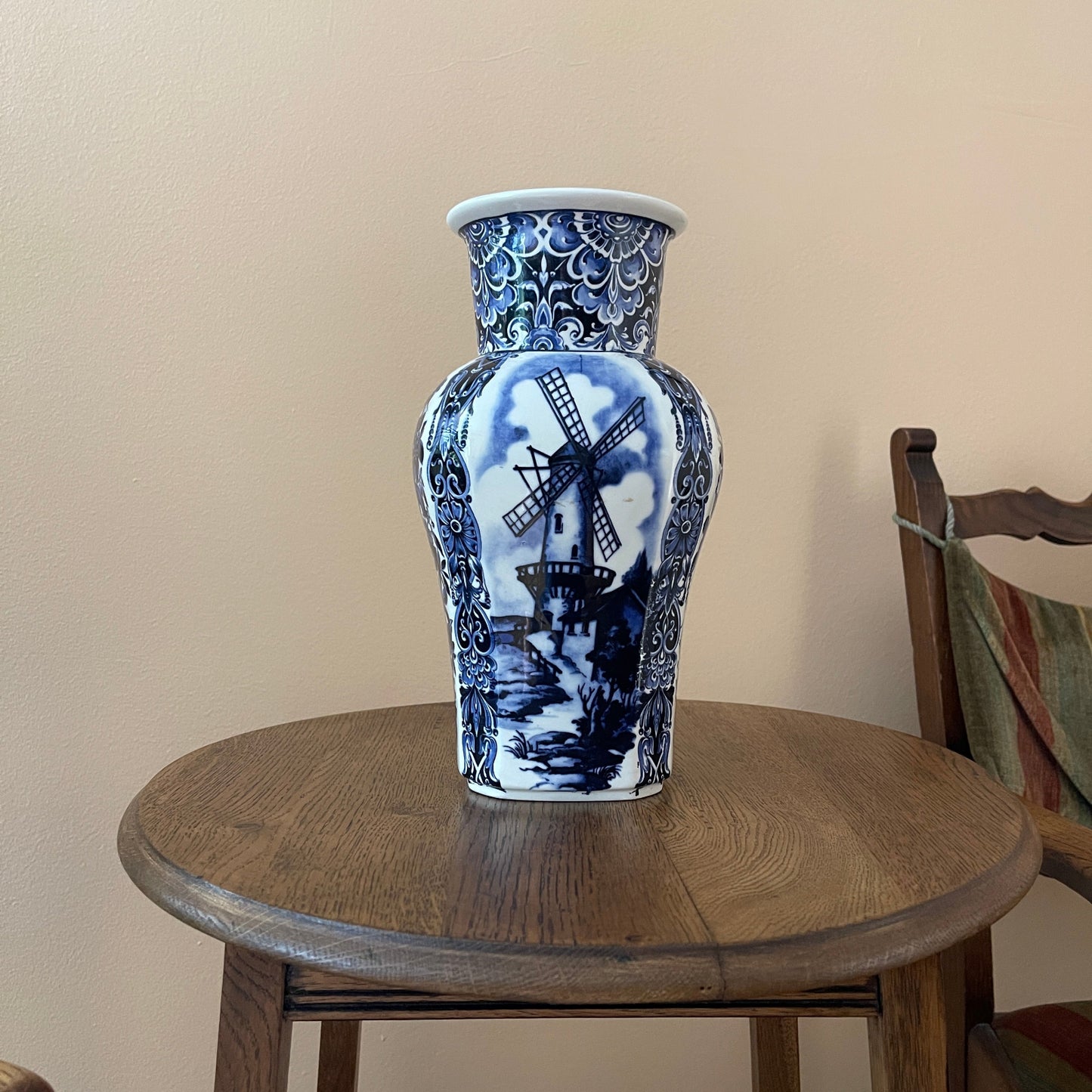 Blue and white ceramic vase with a windmill design on a wooden table against a beige wall.