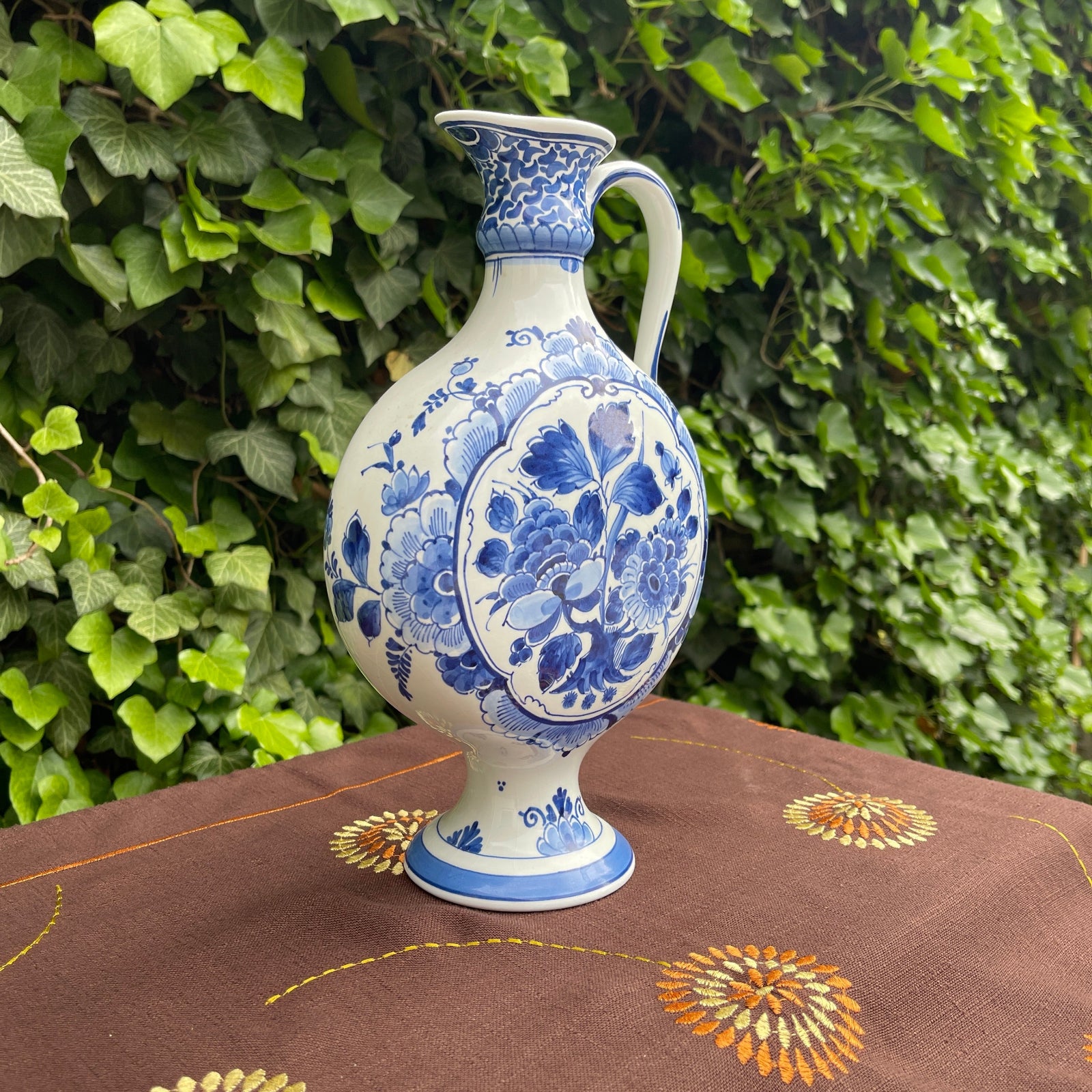 Blue and white floral-patterned vase on a brown fabric surface with green foliage in the background
