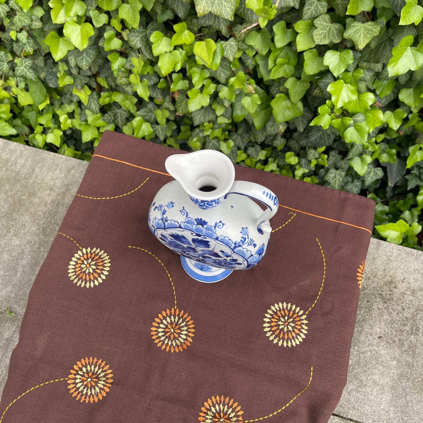 White ceramic teapot with blue floral patterns on a brown fabric with orange and green leafy background