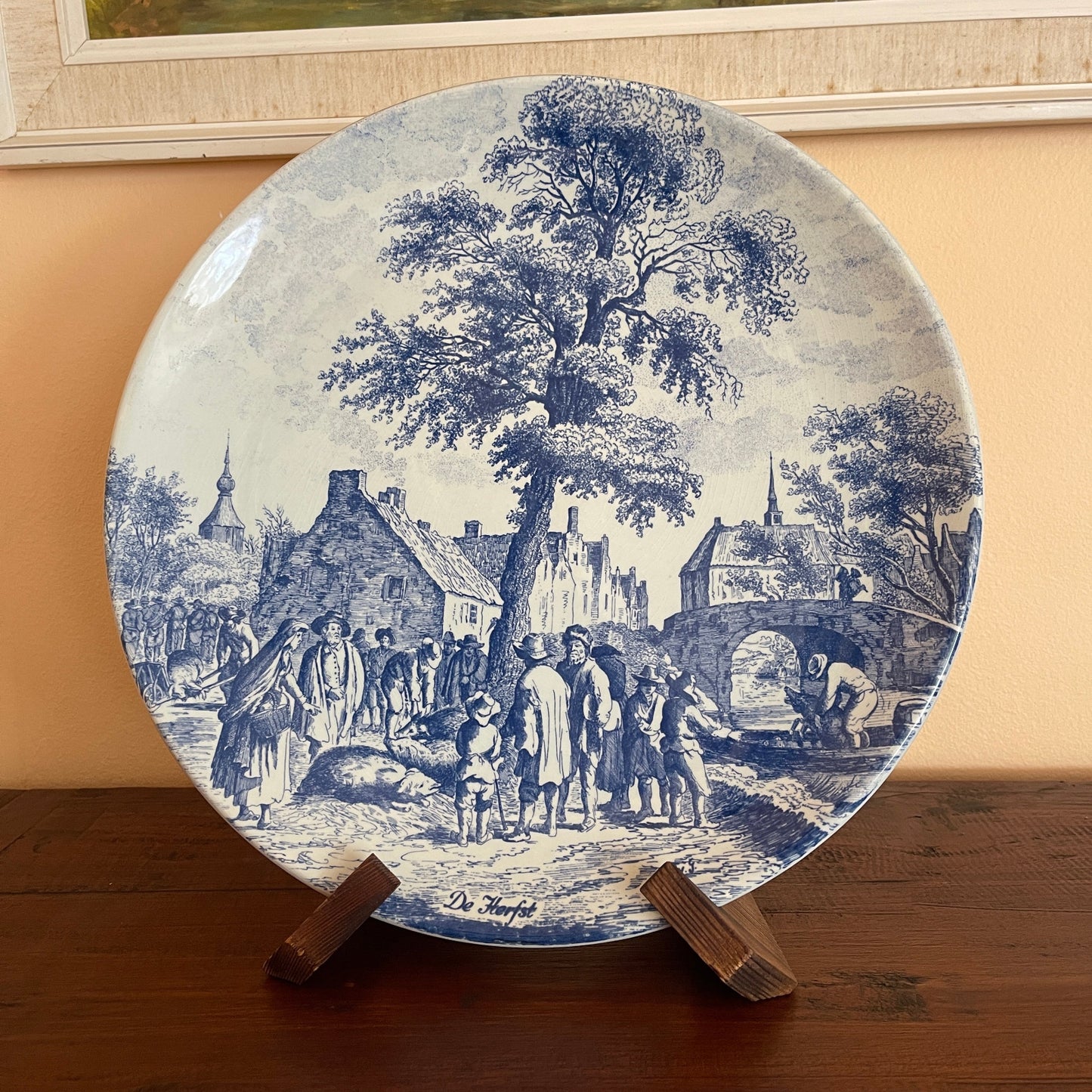 Decorative plate with blue and white vintage scene on a stand against a beige wall.
