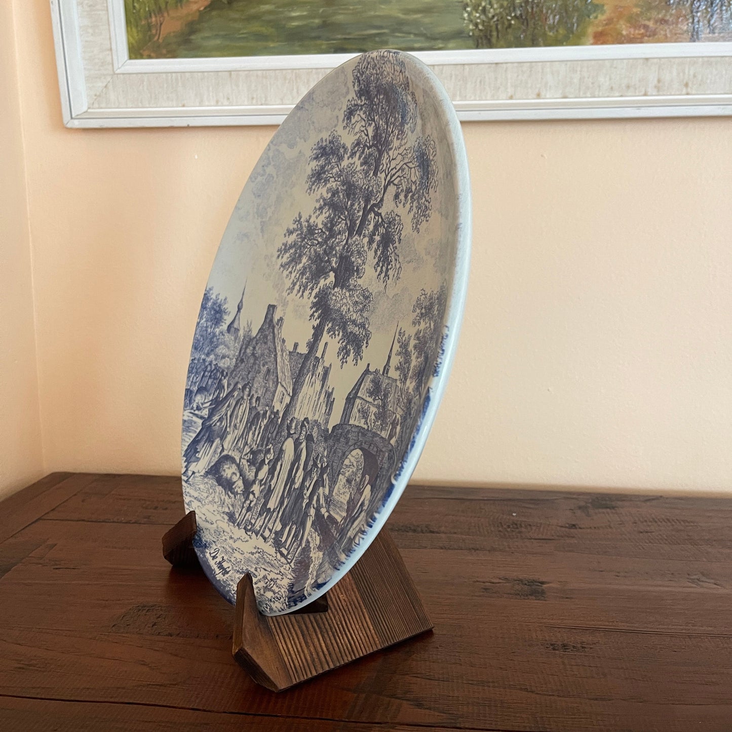 Decorative plate with landscape design on a stand against a wall with a framed picture.