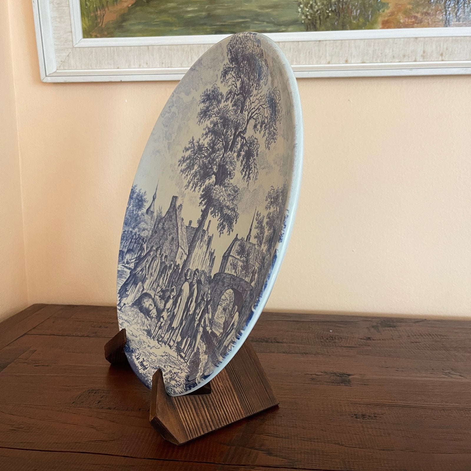 Decorative plate with landscape design on a stand against a wall with a framed picture.