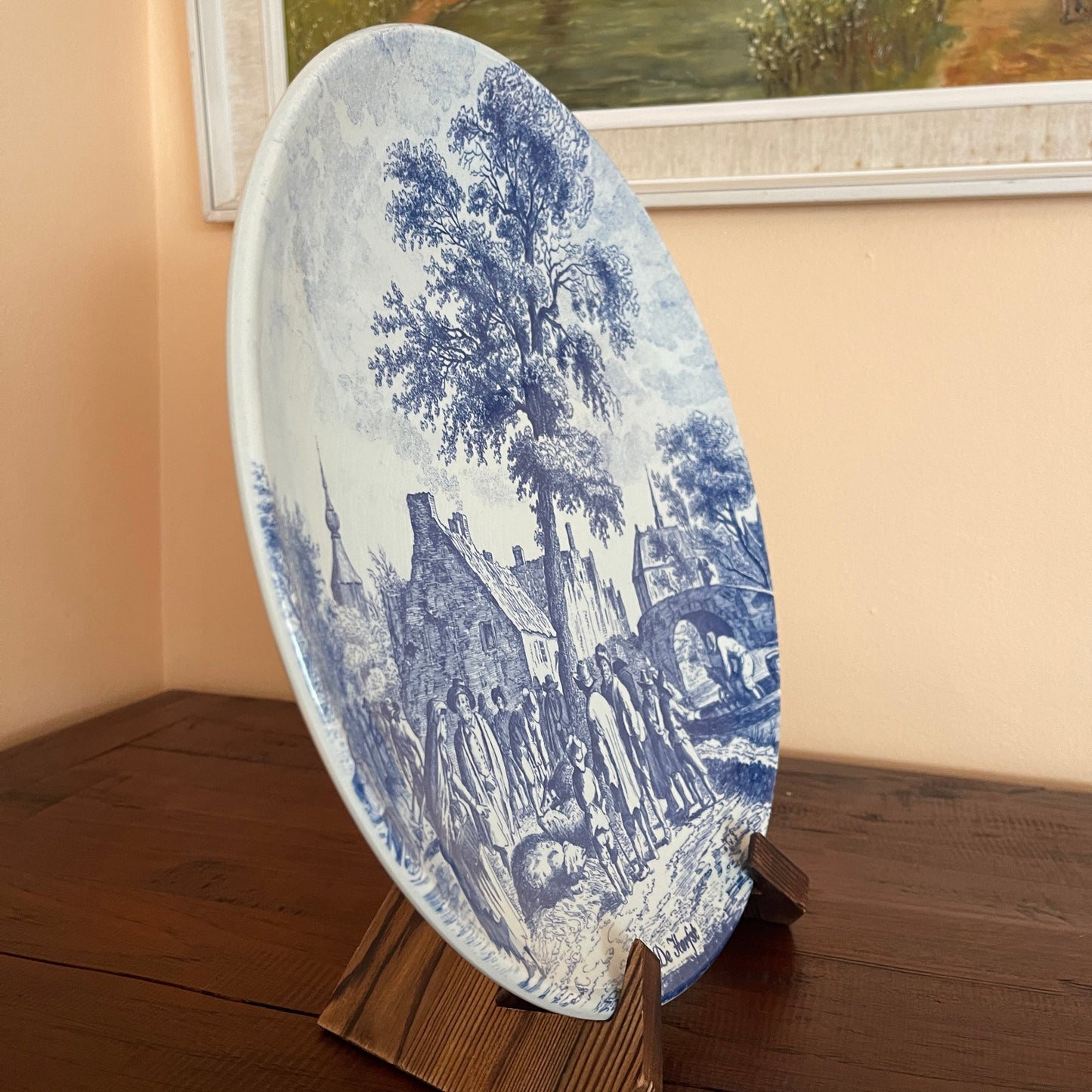 Round blue and white decorative plate with a scenic design on a stand against a beige wall.