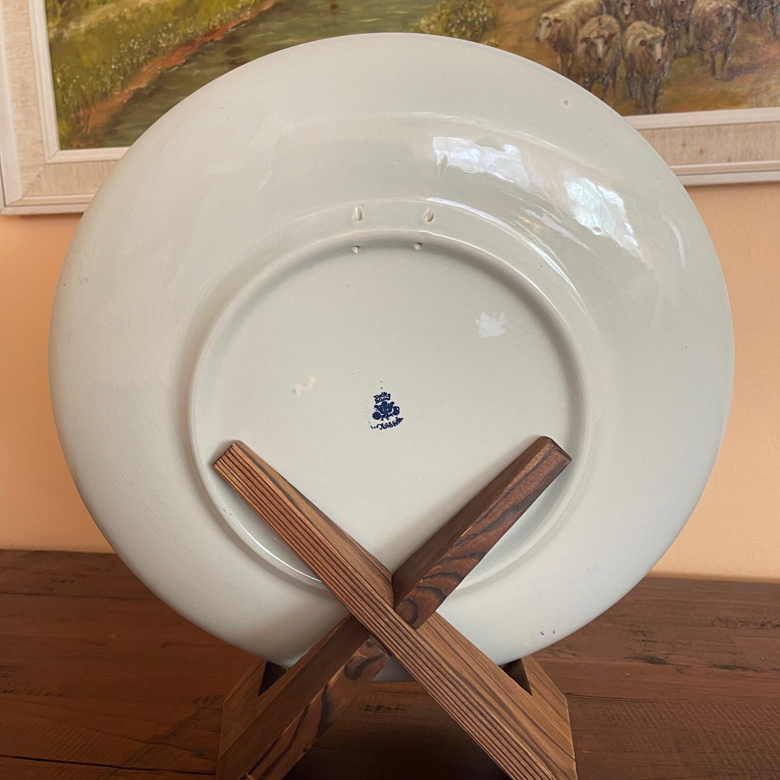 White plate with a blue logo on a wooden stand against a wall with a painting of bears.