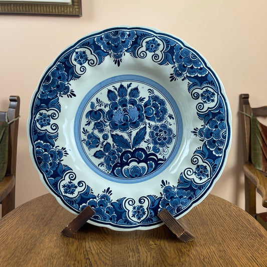 Blue and white floral ceramic plate on a wooden stand against a beige wall.