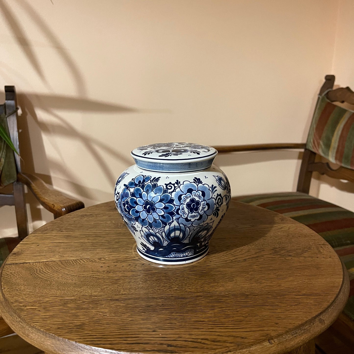 Blue and white floral ceramic jar on a wooden table with a chair and striped cushion in the background.
