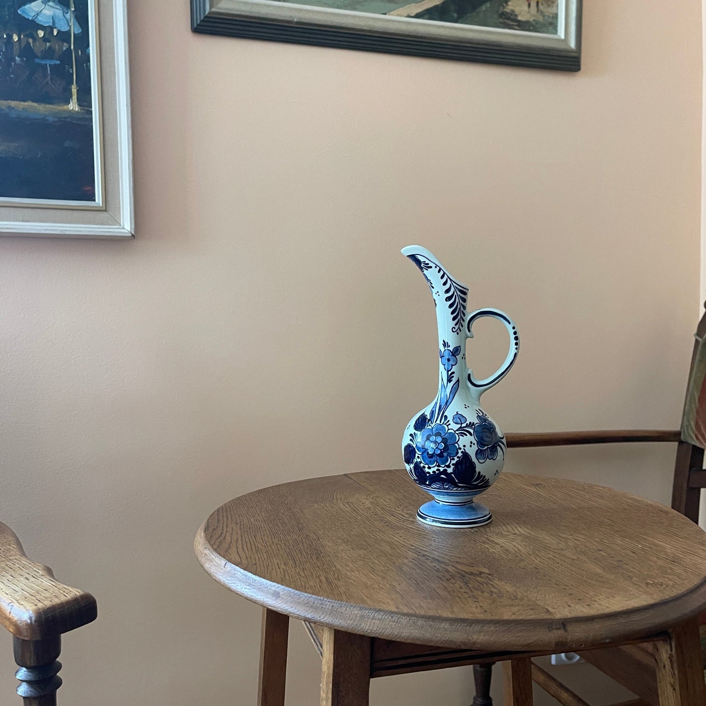 Blue and white ceramic pitcher on a wooden table against a beige wall with framed pictures.