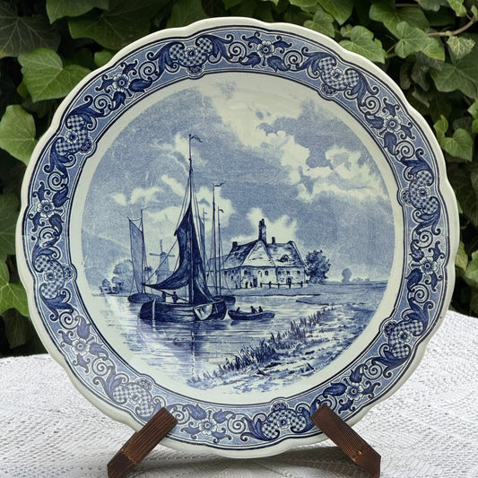 Decorative plate with blue and white scenic design featuring boats and a house, placed on a stand.